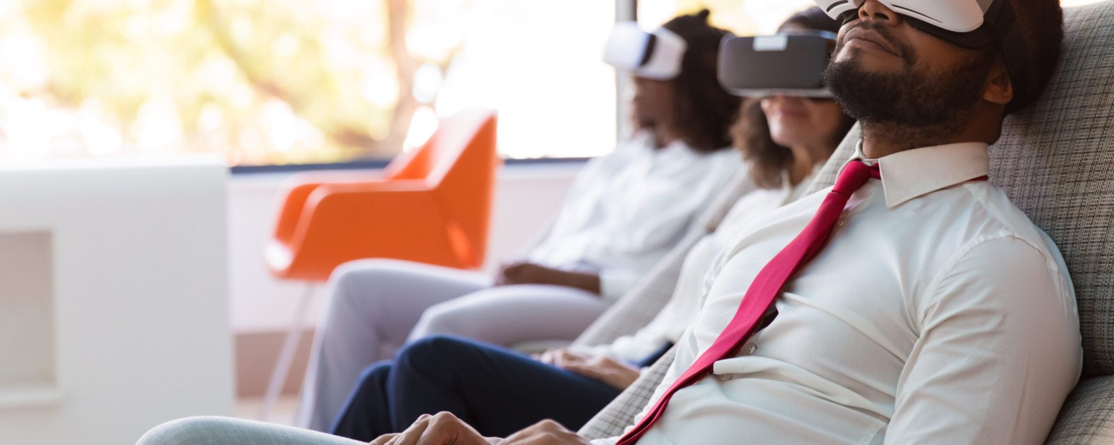 Serene business people enjoying VR experience in studio. Man and women wearing virtual reality headsets, sitting in motion chairs, relaxing and smiling. VR entertainment concept